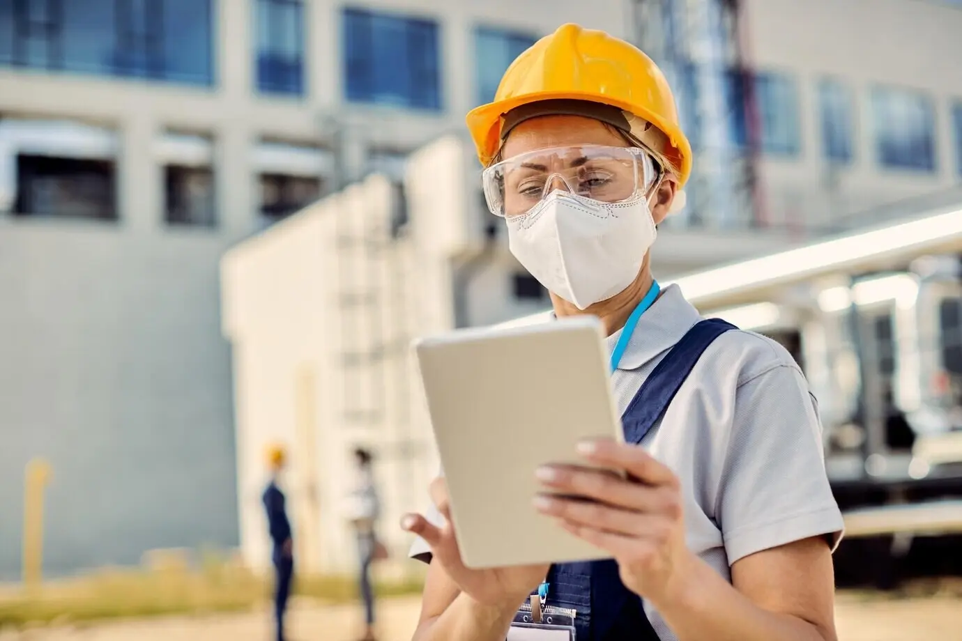 Bauingenieurin oder Bauingenieur mit Schutzmaske arbeitet an einem Touchpad auf der Baustelle.